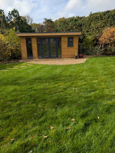 Modern wooden garden shed set on a lawn, surrounded by trees and shrubs.